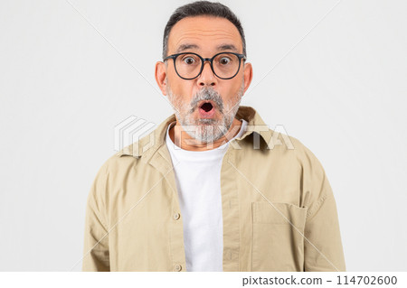 A senior man with a surprised expression on his face, his eyes wide open and mouth slightly agape. He appears shocked or amazed by something he seeing or hearing. 114702600
