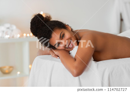 African American woman lies on her stomach at a spa with a relaxed and content smile, looking directly at the camera African American woman lies on her stomach at a spa with a relaxed and content smile, looking directly at the camera 114702727
