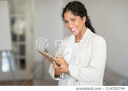 Cheerful young woman medical expert with clipboard prepares for patient visit, showing professionalism and approachability Cheerful young woman medical expert with clipboard prepares for patient visit, showing professionalism and approachability 114702744