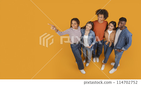 A forward-thinking group of friends look and point upward together, symbolizing goals and aspirations in a multiethnic context, isolated on a yellow background, copy space 114702752