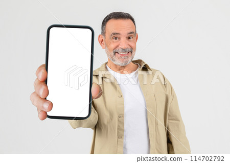 A senior man standing while holding a smart phone in his hand, looking at the screen. The mans face is focused as he interacts with the device, possibly texting, browsing, or taking a call. A senior man standing while holding a smart phone in his hand, looking at the screen. The mans face is focused as he interacts with the device, possibly texting, browsing, or taking a call. 114702792