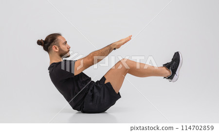 A man dressed in a black shirt and shorts is engaged in a stretching exercise outdoors. He is bending and reaching to increase flexibility and prevent muscle tightness. A man dressed in a black shirt and shorts is engaged in a stretching exercise outdoors. He is bending and reaching to increase flexibility and prevent muscle tightness. 114702859