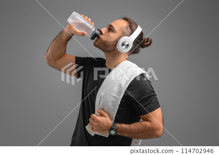A man is seen wearing headphones as he takes a sip from a water bottle. He appears to be enjoying a refreshment while listening to music through his headphones. A man is seen wearing headphones as he takes a sip from a water bottle. He appears to be enjoying a refreshment while listening to music through his headphones. 114702946