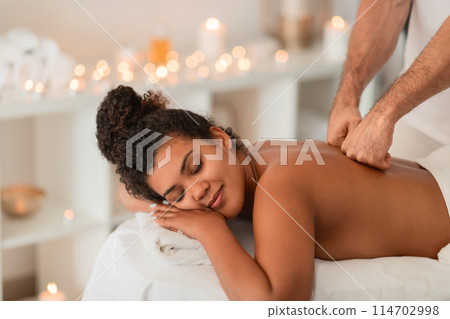 A peaceful African American lady enjoys a blissful spa session, emphasizing the relaxation and care provided to people at wellness centers 114702998