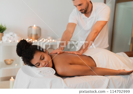 A dedicated massage therapist attentively assists an african american lady at a spa, capturing relaxation and professional service 114702999