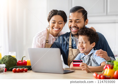 Happy African American family father mother and preteen son with laptop and credit card in kitchen, buying grocery online 114703000