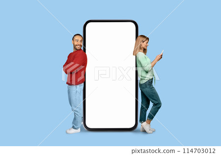 A man and woman stand back-to-back with a giant, blank smartphone screen between them on a blue background 114703012