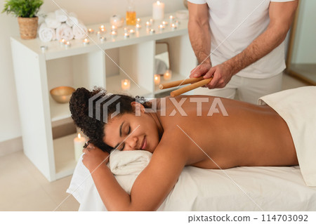 A spa therapist utilizes singing bowls for a sound therapy session with a peaceful African American lady, enhancing the holistic experience for people 114703092