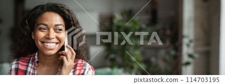 Portrait of cheerful black young woman calling by phone, talking with friend in minimalist living room interior, close up. Communication remotely at device, gossip and good news, copy space, banner Portrait of cheerful black young woman calling by phone, talking with friend in minimalist living room interior, close up. Communication remotely at device, gossip and good news, copy space, banner 114703195