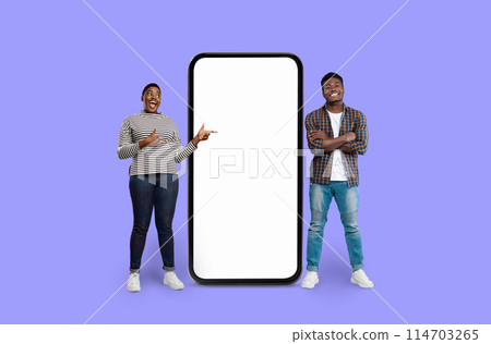 Two people African American man and woman gesturing towards a large-scale smartphone mockup on violet 114703265