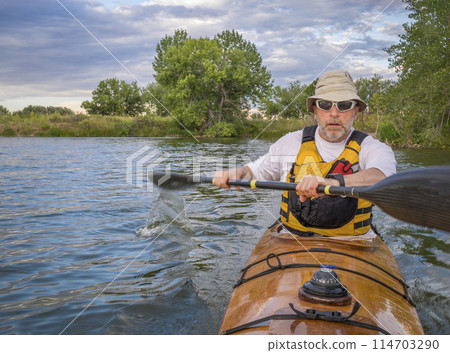 bow view of a senior male paddling a home built wooden sea kayak on a lake in Colorado 114703290