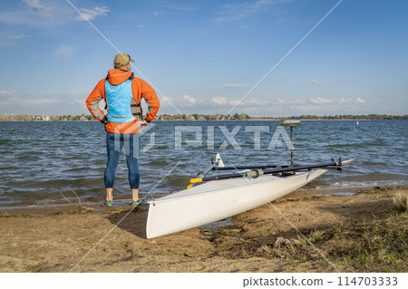 Senior male rower with his rowing shell on a beach of Boyd Lake in northern Colorado, early spring scenery Senior male rower with his rowing shell on a beach of Boyd Lake in northern Colorado, early spring scenery 114703333