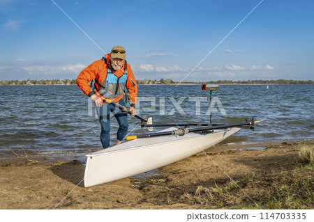 Senior male rower with his rowing shell on a beach of Boyd Lake in northern Colorado, early spring scenery Senior male rower with his rowing shell on a beach of Boyd Lake in northern Colorado, early spring scenery 114703335