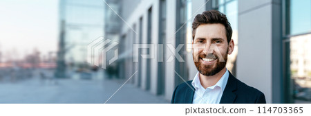 Portrait of smiling confident attractive millennial businessman with beard in suit looking at camera near office building, outdoor, copy space. Ceo manager and boss, successful work, career, business Portrait of smiling confident attractive millennial businessman with beard in suit looking at camera near office building, outdoor, copy space. Ceo manager and boss, successful work, career, business 114703365