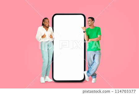 African American man giving thumbs up and woman smiling beside an empty screen on a pink backdrop, ideal for advertisements 114703377