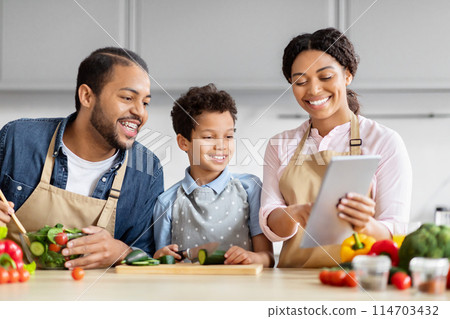 African American family shares a tablet while cooking in a kitchen, focusing on healthy food recipes African American family shares a tablet while cooking in a kitchen, focusing on healthy food recipes 114703432