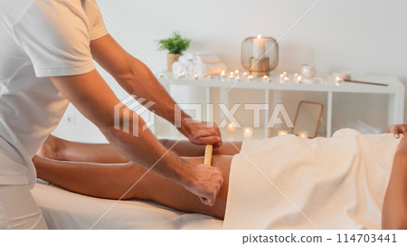 A serene massage room setting with a professional masseuse providing a calming back massage to a client covered with a towel. The atmosphere suggests tranquility and luxury 114703441