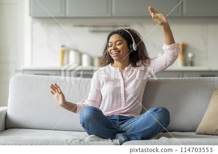 An african american lady is captured in a moment of joy while listening to music with headphones in her home 114703553