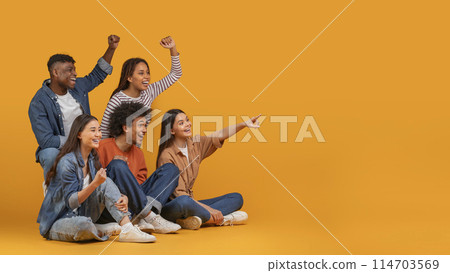 Multiethnic friends excitedly cheering and pointing to the side, exemplifying celebration and happiness in a diverse group, isolated on a yellow background, copy space 114703569
