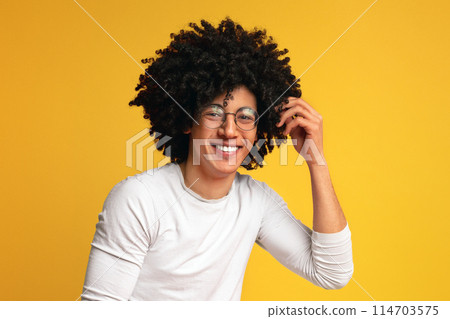 Carefree black guy in glasses with bushy hairstyle laughing and touching his head, orange studio background, sincere human emotions 114703575