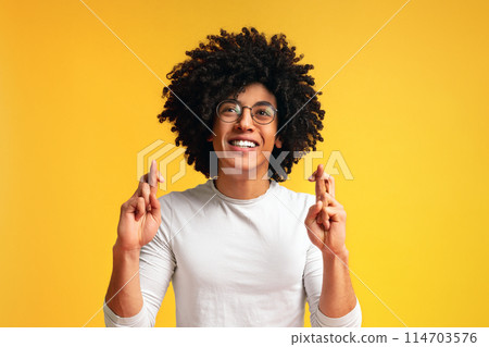 Positive african-american guy crossing fingers, making wish, hopes for fortune and good luck, orange background 114703576