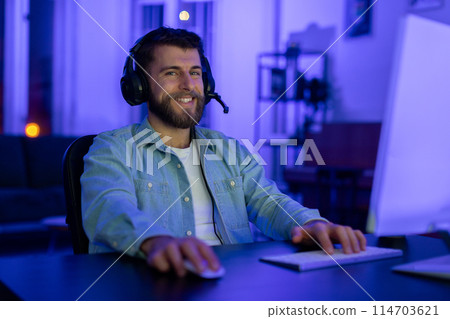 A content millennial guy with a welcoming smile, engaging in gaming at his home setup, representing the social and addictive aspects of gaming A content millennial guy with a welcoming smile, engaging in gaming at his home setup, representing the social and addictive aspects of gaming 114703621