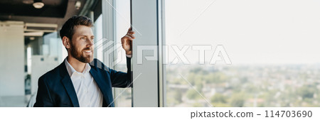 Confident business man in suit standing in modern coworking office room, leaning on window, looking away and smiling, free copy space, web-banner Confident business man in suit standing in modern coworking office room, leaning on window, looking away and smiling, free copy space, web-banner 114703690