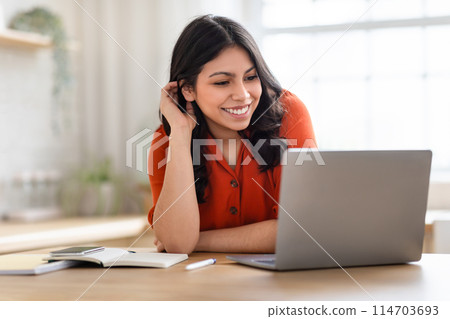 A focused middle eastern woman learning or working on a laptop at home, embodies a modern educational setting 114703693