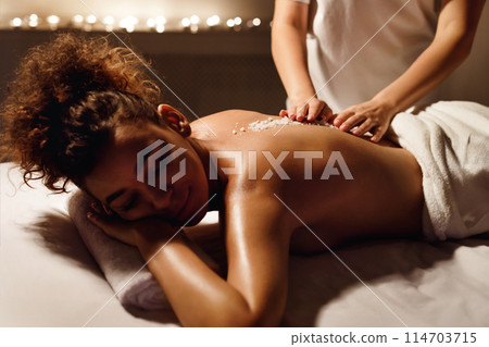 African american woman enjoys a soothing back massage in a serene spa setting with dim lighting and candles in the background 114703715