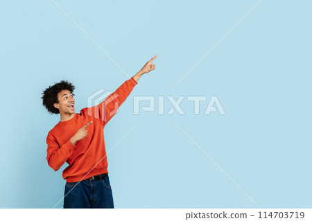 African american guy in casual attire expressing joy and pointing upwards on the blue isolated background, representing the concept of success or discovery, copy space 114703719