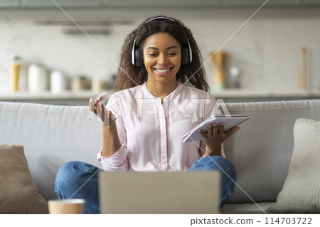 African American woman smiles engagingly while video conferencing from home, her headphones suggest an immersive call 114703722