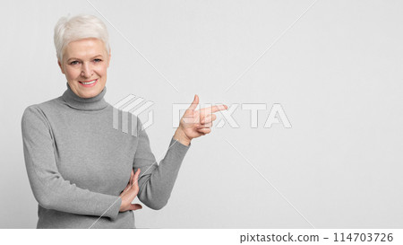This image shows an elderly European woman pointing to the side, a gesture that can convey direction or sharing information in a s3niorlife context 114703726