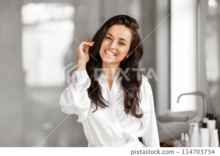 A playful lady strikes a charming pose in a bathroom setting, signifying millennial enjoyment of skin care and life 114703734