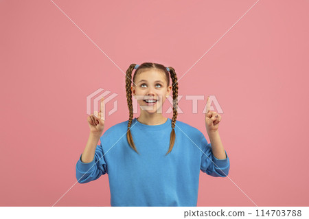 A cheerful young girl with braided hair points upwards, smiling on a pink background, showing enthusiasm and curiosity, copy space A cheerful young girl with braided hair points upwards, smiling on a pink background, showing enthusiasm and curiosity, copy space 114703788