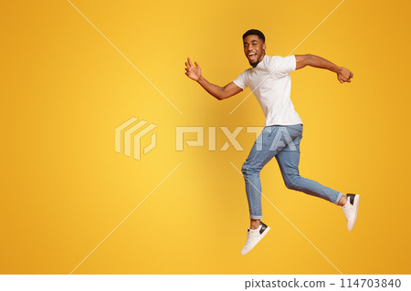 Joyful millennial african-american guy walking on air, jumping on orange studio background, smiling at camera 114703840