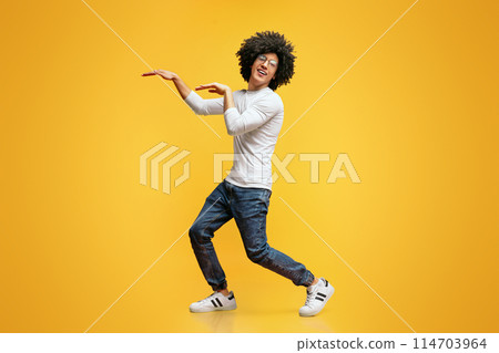 Funny black guy fooling, dancing in egypt style on orange studio background 114703964