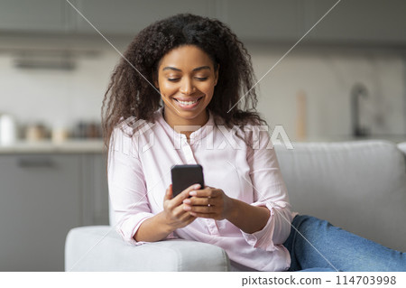 An african american lady is seen comfortably texting on her smartphone, providing a glimpse into home life and millennial habits 114703998