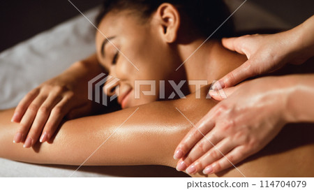 African-american girl enjoying shoulder massage in the health spa, closeup 114704079