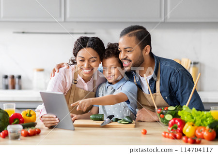 African American couple with their child using a tablet while cooking in a family kitchen environment African American couple with their child using a tablet while cooking in a family kitchen environment 114704117