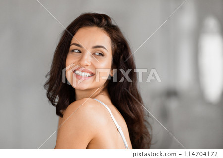 Cheerful lady glances back with a radiant smile, embodying optimism in a grayscale bathroom scene, copy space Cheerful lady glances back with a radiant smile, embodying optimism in a grayscale bathroom scene, copy space 114704172