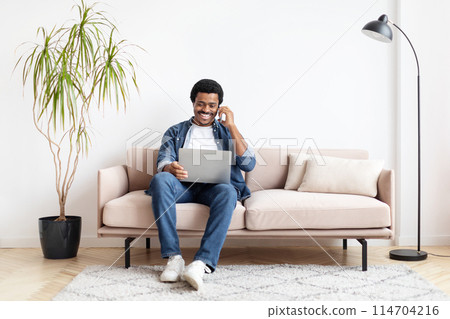 Relaxed african american guy at home multitasking with a laptop and phone, connoting work-life balance Relaxed african american guy at home multitasking with a laptop and phone, connoting work-life balance 114704216