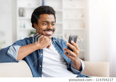 A jovial black man shares something amusing on his mobile screen, encapsulating the essence of connectivity at home A jovial black man shares something amusing on his mobile screen, encapsulating the essence of connectivity at home 114704217