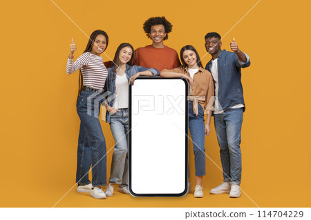 An international team of friends surrounds a large blank smartphone screen, depicting a concept of a connected, multiethnic, and multiracial team isolated on orange An international team of friends surrounds a large blank smartphone screen, depicting a concept of a connected, multiethnic, and multiracial team isolated on orange 114704229