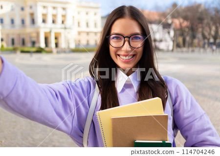 A millennial lady with glasses takes a joyful selfie outdoors, portraying a vibrant student life in a European setting A millennial lady with glasses takes a joyful selfie outdoors, portraying a vibrant student life in a European setting 114704246