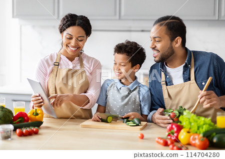 An African American family using a tablet for recipes while cooking a healthy meal at home, checking food blog 114704280