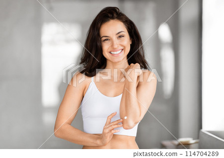 A cheerful, fit woman in a white tank top poses with one arm raised, radiating confidence and health, body care concept 114704289