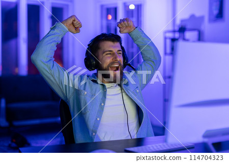 The image captures the thrill and addictive nature of gaming as a young millennial guy celebrates at home, symbolizing victory The image captures the thrill and addictive nature of gaming as a young millennial guy celebrates at home, symbolizing victory 114704323