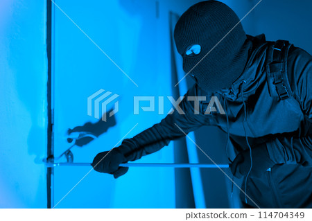 A caught-in-action shot of a thief cautiously opening a glass door while exiting, denoting the silent danger of burglary at an apartment at night A caught-in-action shot of a thief cautiously opening a glass door while exiting, denoting the silent danger of burglary at an apartment at night 114704349