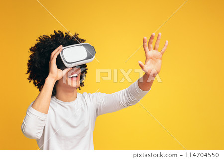 Enjoying cyberspace. Excited black guy pushing virtual button in VR glasses, orange background 114704550