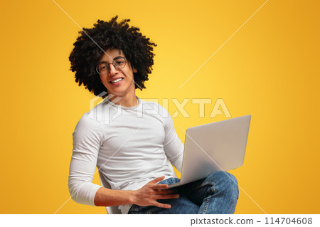 Online education. Cheerful african american guy watching webinar on laptop, orange background Online education. Cheerful african american guy watching webinar on laptop, orange background 114704608